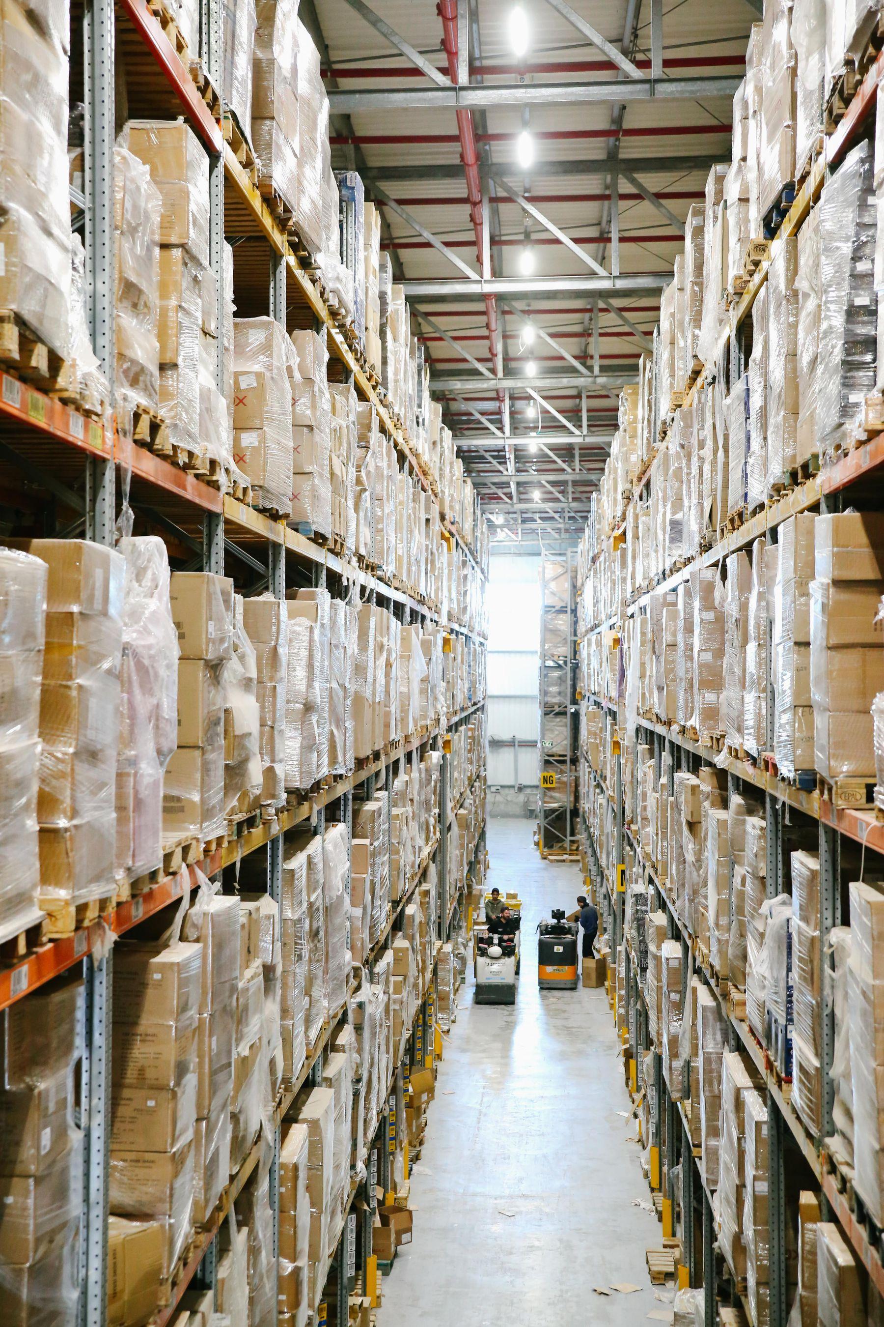 Illustrated wholesale warehouse shelves with cartons, small goods, and a packing table